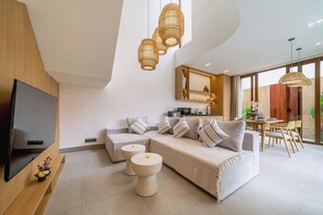 A modern living room with a sofa, two round side tables, a flat-screen TV, and a dining area with a table and chairs. - New Chic Berawa Villa • Pool • 2BR • Walk to Beach (Kabupaten Badung)