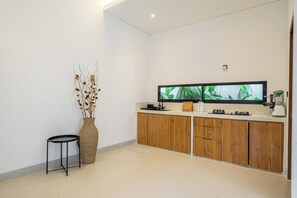 A modern kitchen with wooden cabinets, a black countertop, and a large flat-screen TV mounted above the counter. - New Designer 2BR Villa+Huge Pool+Central Location (Kuta Utara)