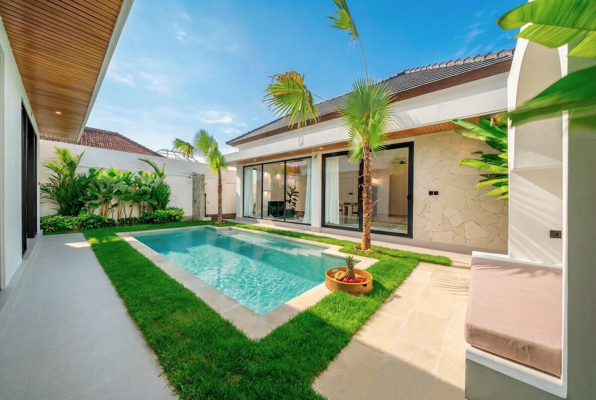 A modern house with a swimming pool, a patio with a cushioned seating area, and a well-maintained garden.
