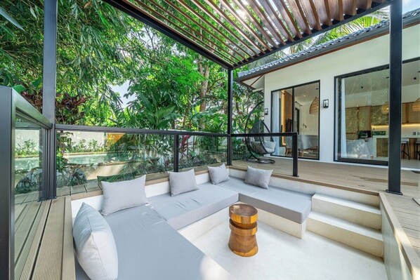 A modern outdoor seating area with a wooden table, cushioned seating, and a view of a lush garden. - Ubud 2BR Escape w/Pool! Caffes & Nature Nearby (Gianyar Regency)