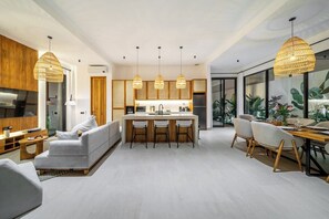 Een moderne keuken met hanglampen, een eethoek met een houten tafel en stoelen, en een woonkamer met een bank en televisie.