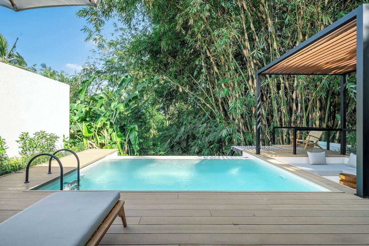 En swimmingpool med en træterrasse, omgivet af frodig vegetation og et moderne udendørs opholdsområde.