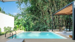 Una piscina con bordo in legno, circondata da vegetazione rigogliosa e un'area salotto esterna dal design moderno.