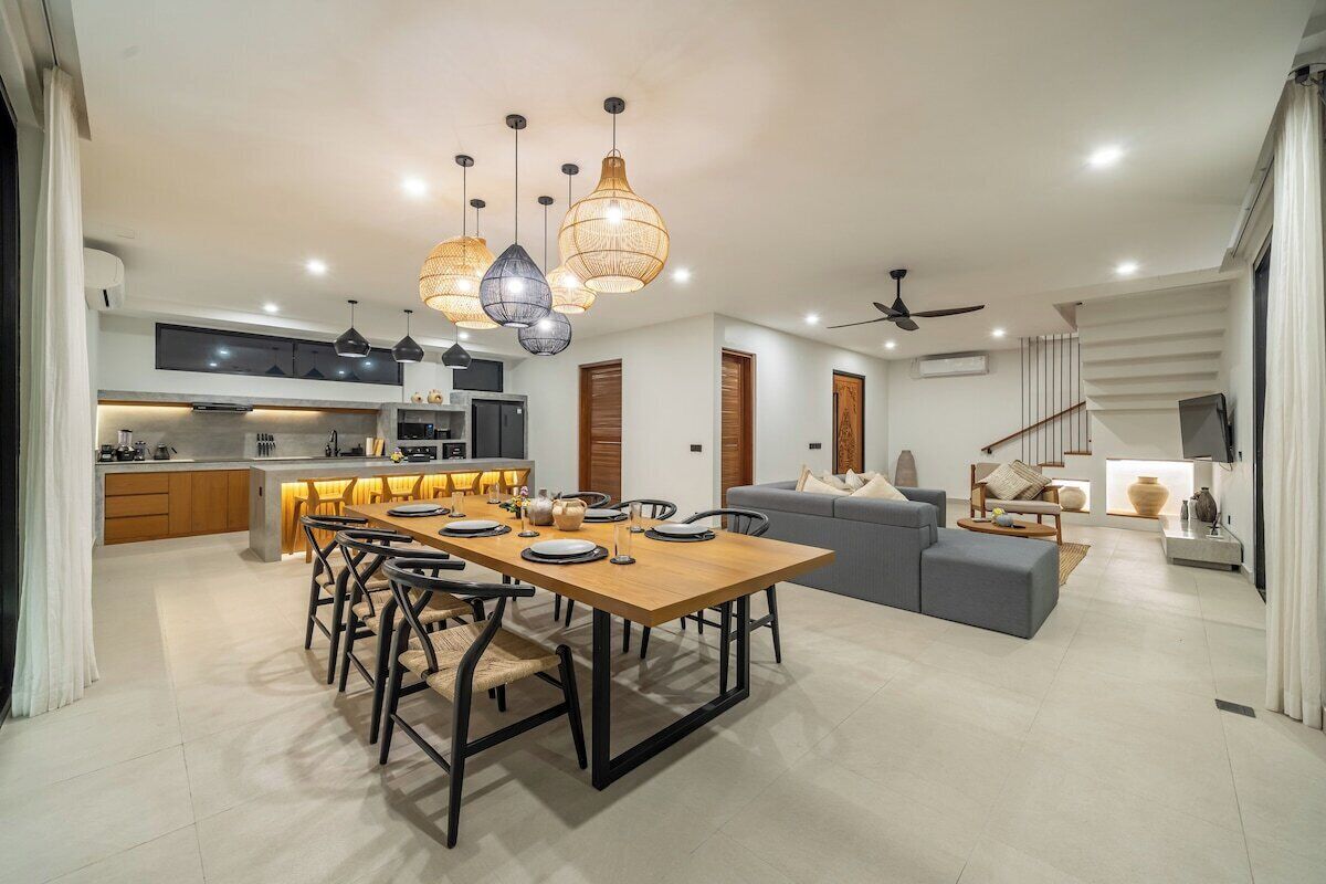 A modern kitchen with a dining area, a grey sofa, and a staircase.
