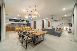 A modern kitchen with a dining area, a grey sofa, and a staircase. - Serene 3BR Escape w Beach Nearby, Huge Pool&Garden (Kabupaten Badung)