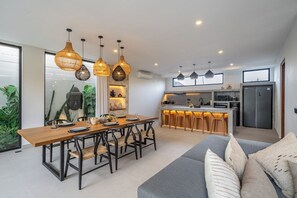 Une cuisine moderne dotée d’un îlot central, de luminaires suspendus et d’un coin repas avec une table et des chaises en bois.