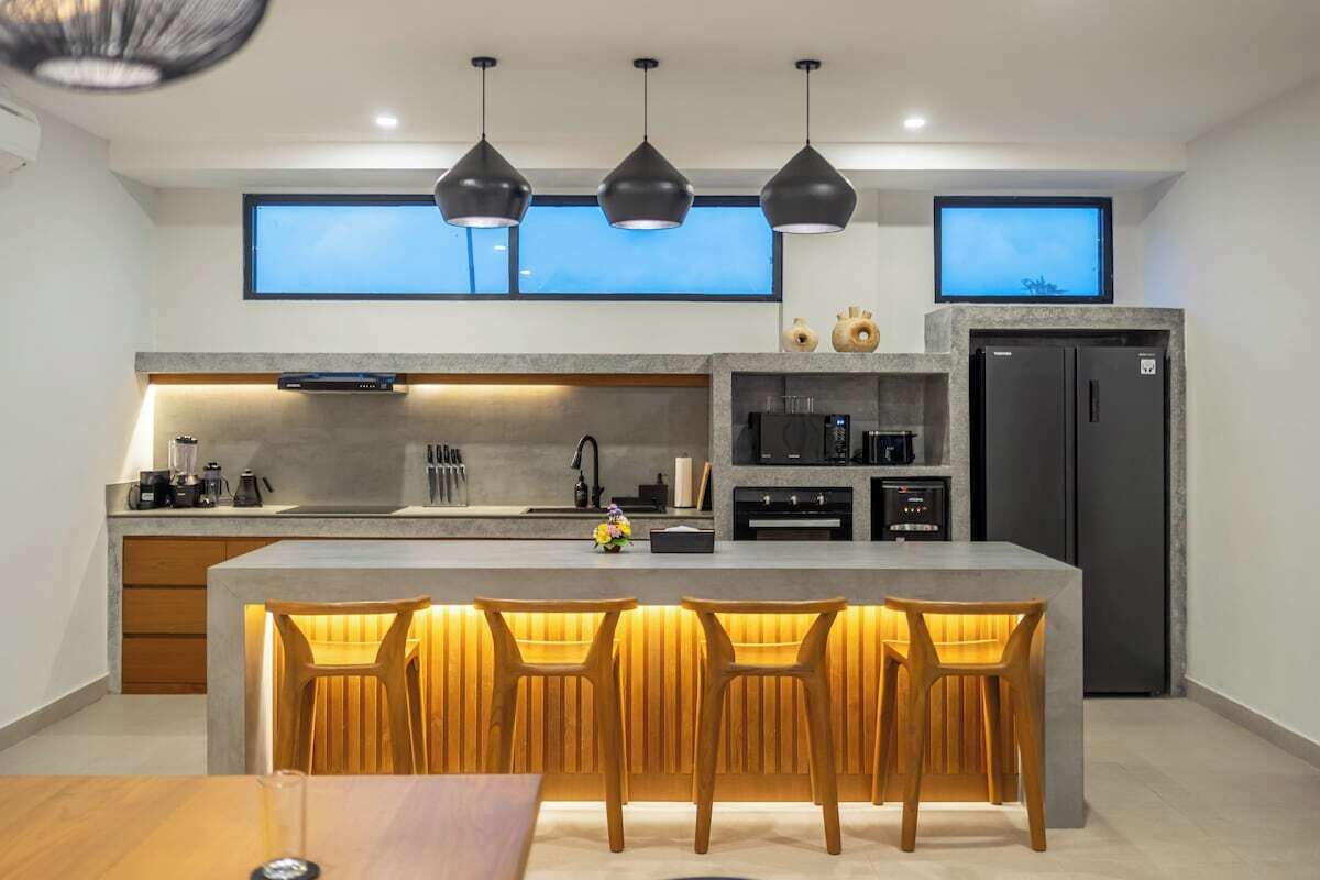 A modern kitchen with a central island, bar stools, pendant lighting, and a built-in oven.