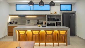 Una cucina moderna con isola centrale, sgabelli da bar, illuminazione a sospensione e forno integrato.