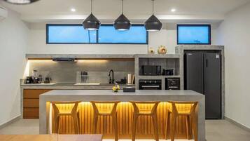 A modern kitchen with a central island, bar stools, pendant lighting, and a built-in oven.