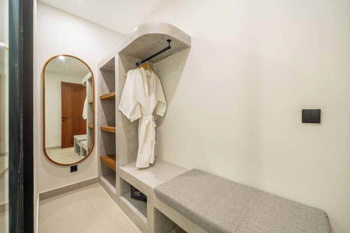 A bathroom with a bench, a robe rack, and a mirror.