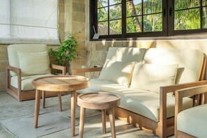 Una habitación con un sofá y dos mesas de madera, una planta en maceta y una ventana con vista a palmeras.