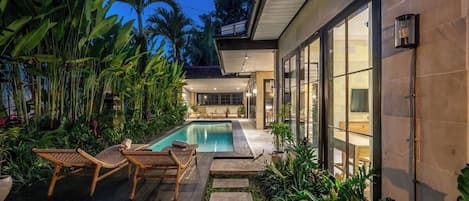 A modern house with a swimming pool, outdoor seating, and lush greenery.