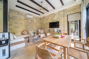 A modern living room with a wooden dining table, sofas, a TV, and a refrigerator. - Cozy Ubud's 2BR Escape with Huge Pool & Patio (Ubud)