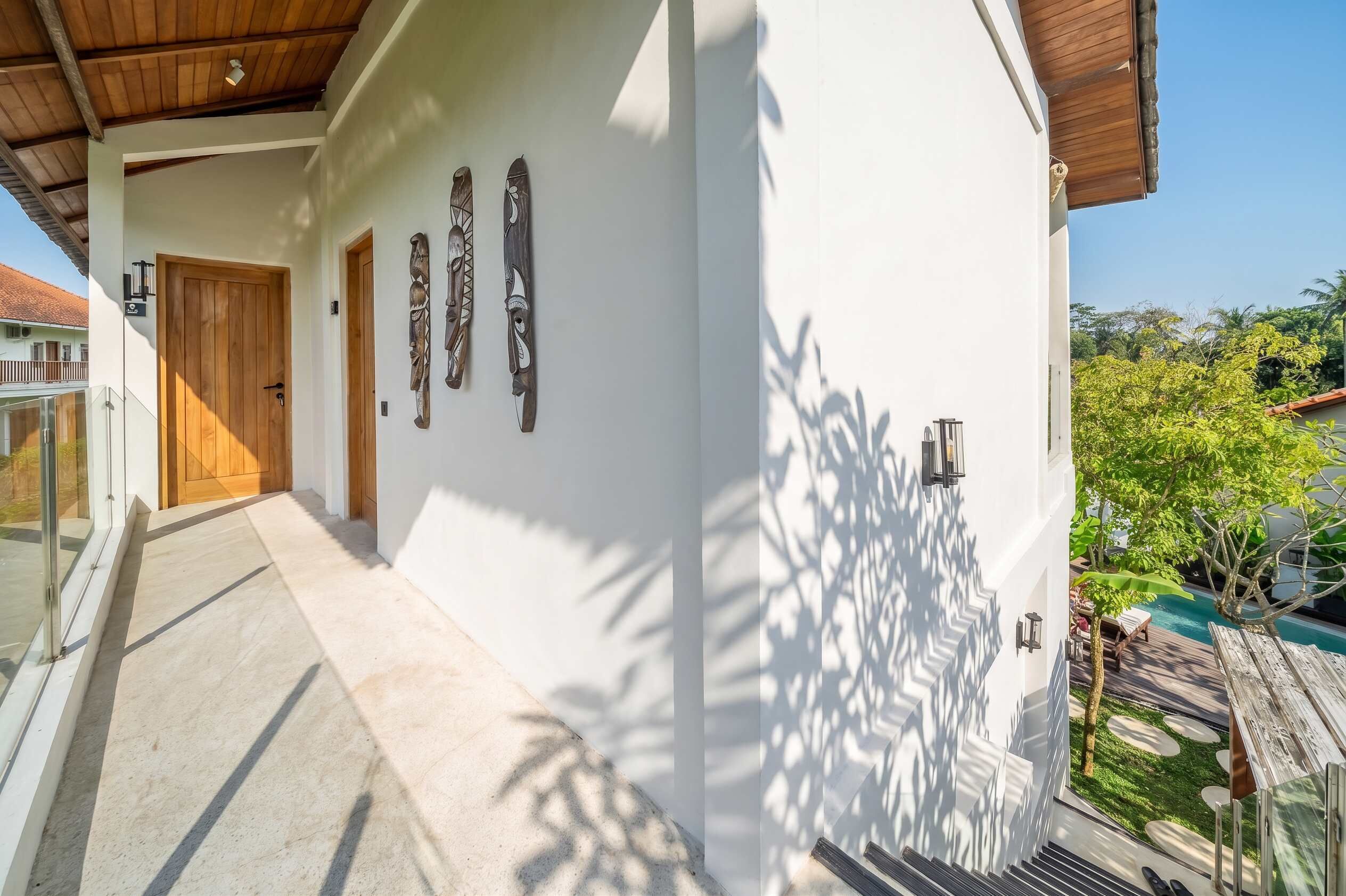 Ein modernes Gebäude mit weißer Fassade, einer Holztür und einem Balkon mit Pool.
