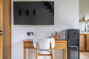 Ett kök med en stor tv-skärm på väggen, ett träbord med en stol och ett svart kylskåp.