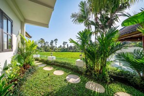 A well-maintained garden with a pathway, palm trees, and a view of a rice field. - Tropical 1BR w Private Pool&Kitchen in Ubud (Gianyar Regency)