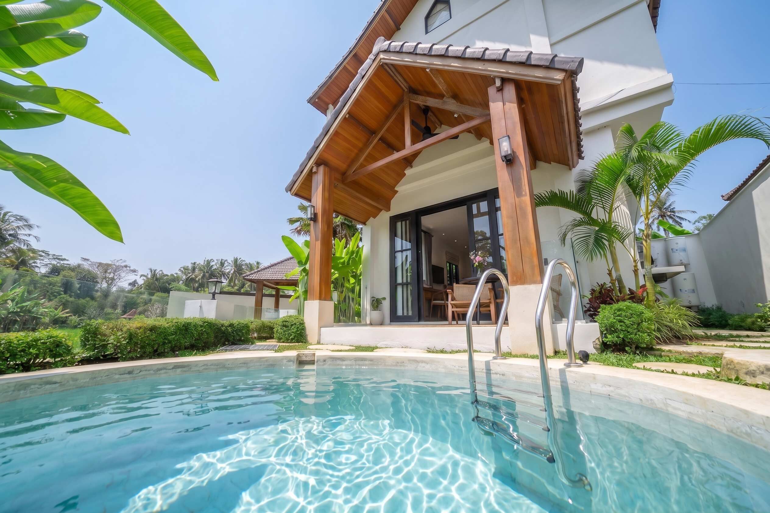 Area piscina con tettoia in legno, piscina azzurra e limpida e edificio bianco con ampie finestre.