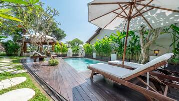 Une terrasse en bois avec une piscine, des chaises longues et une structure surmontée d’un toit de chaume.