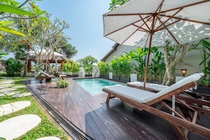 Eine Holzterrasse mit Pool, Liegestühlen und einer strohgedeckten Struktur.