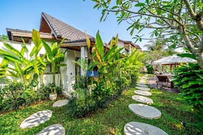 Ein Haus mit Ziegeldach, umgeben von üppiger Vegetation und einem Steinweg, der zu einer Sitzgelegenheit führt.