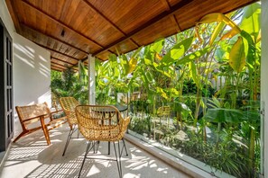 A covered outdoor seating area with wicker chairs and a table, surrounded by lush tropical plants. - Cozy Ubud 1BR w Open-Air Bath, Pool & Gazebo (Gianyar Regency)