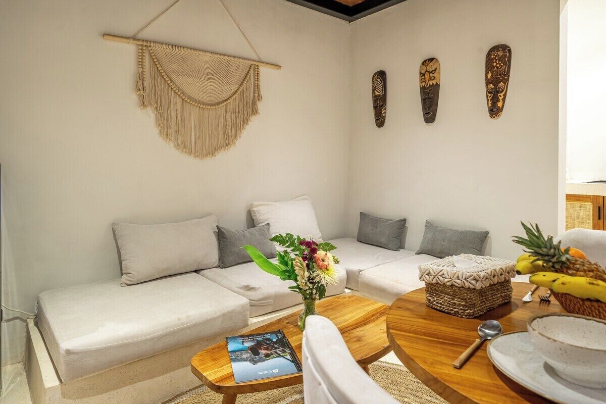 A living room with a sofa, a coffee table, and decorative items including a macrame wall hanging and three wooden masks.