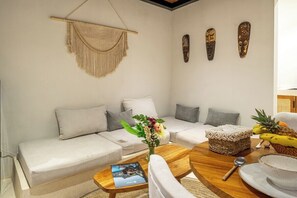 Een woonkamer met een bank, een bijzettafeltje en decoratieve objecten, waaronder een macramé wanddecoratie en drie houten maskers.