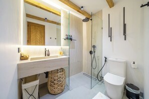 Een moderne badkamer met een houten plafond, een glazen douchecabine, een wit toilet en een wastafel met een spiegel erboven.