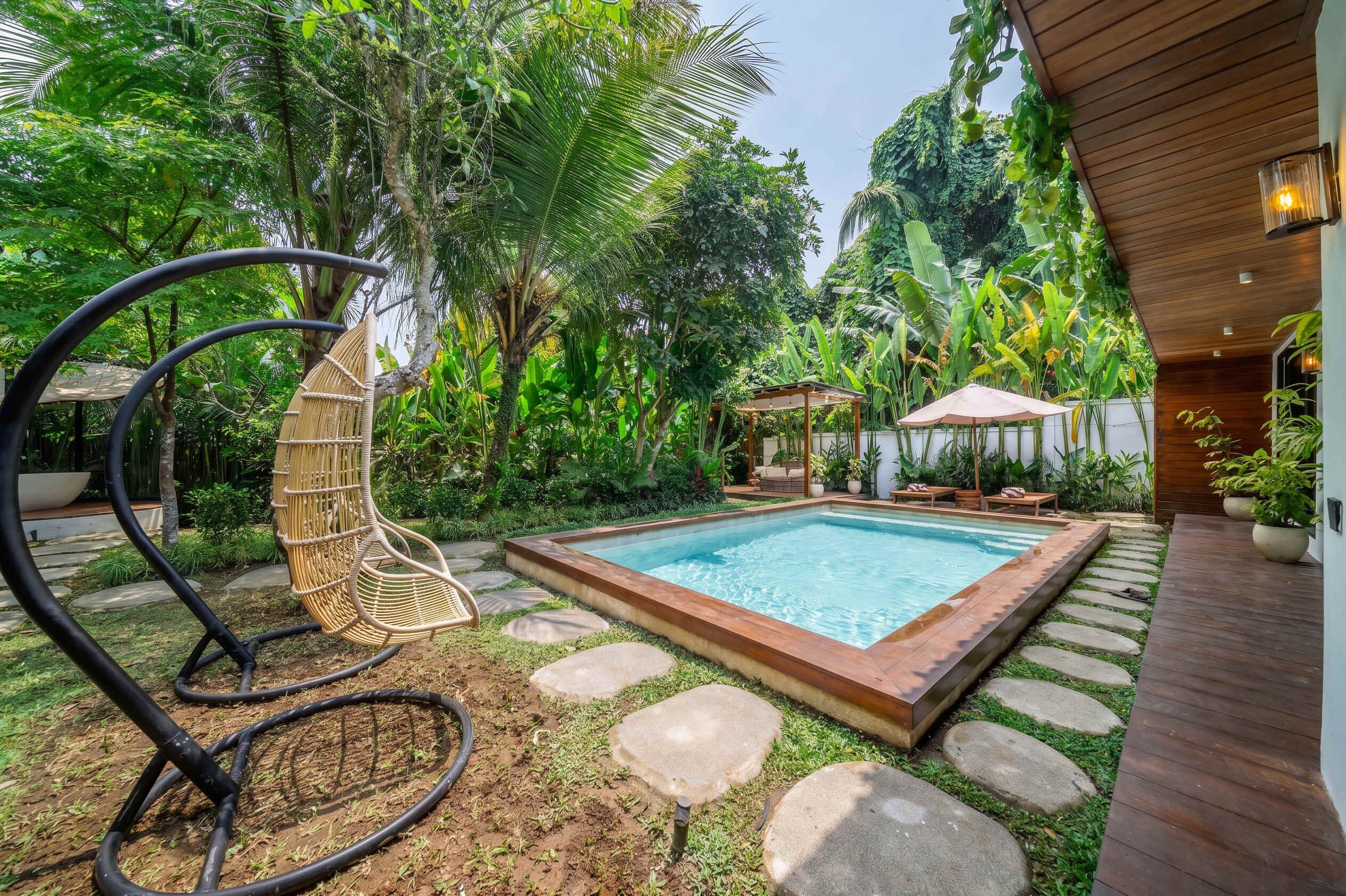 Una piscina rodeada de escalones de piedra, una terraza de madera y exuberante vegetación tropical.