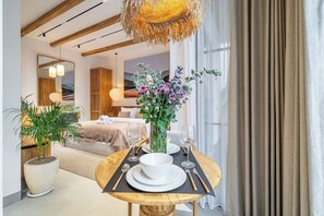 A hotel room with a dining area, a bed, a large window, and a hanging light fixture. - Cozy 1BR • Pool&Garden View • Patio • Central Ubud (Ubud)