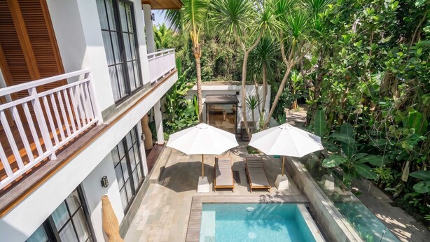 Un área de piscina con vista despejada, dos sombrillas y una tumbona.
