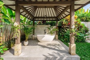 A covered outdoor area with a large white bathtub, surrounded by various plants and a pergola structure. - Cozy 1BR in Lush Ubud w Garden Bath • Pool • Patio (Gianyar Regency)