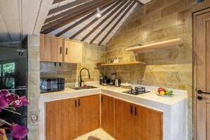 A kitchen with stone walls, wooden cabinets, a built-in microwave, and a gas stove. - Cozy 1BR in Lush Ubud w Garden Bath • Pool • Patio (Gianyar Regency)