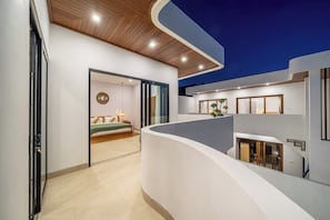 Ein modernes Interieur mit einer gewölbten weißen Wand, einer Holzbalkendecke und einem sichtbaren Schlafzimmer mit Bett und Nachttisch.