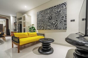 Ein modernes Wohnzimmer mit einem gelben Sofa, einem runden schwarzen Tisch und einem großen, abstrakten Wandbild.