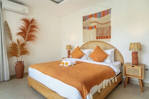 A bedroom with a wooden bed, white bedding, a decorative wall hanging, and two bedside lamps. - Unique 2BR • Beach Nearby • Large Pool • Canggu (Badung Regency)