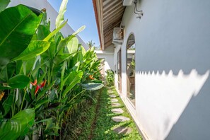 A pathway flanked by lush tropical plants leading to a white building with a covered entrance. - Unique 2BR • Beach Nearby • Large Pool • Canggu (Badung Regency)