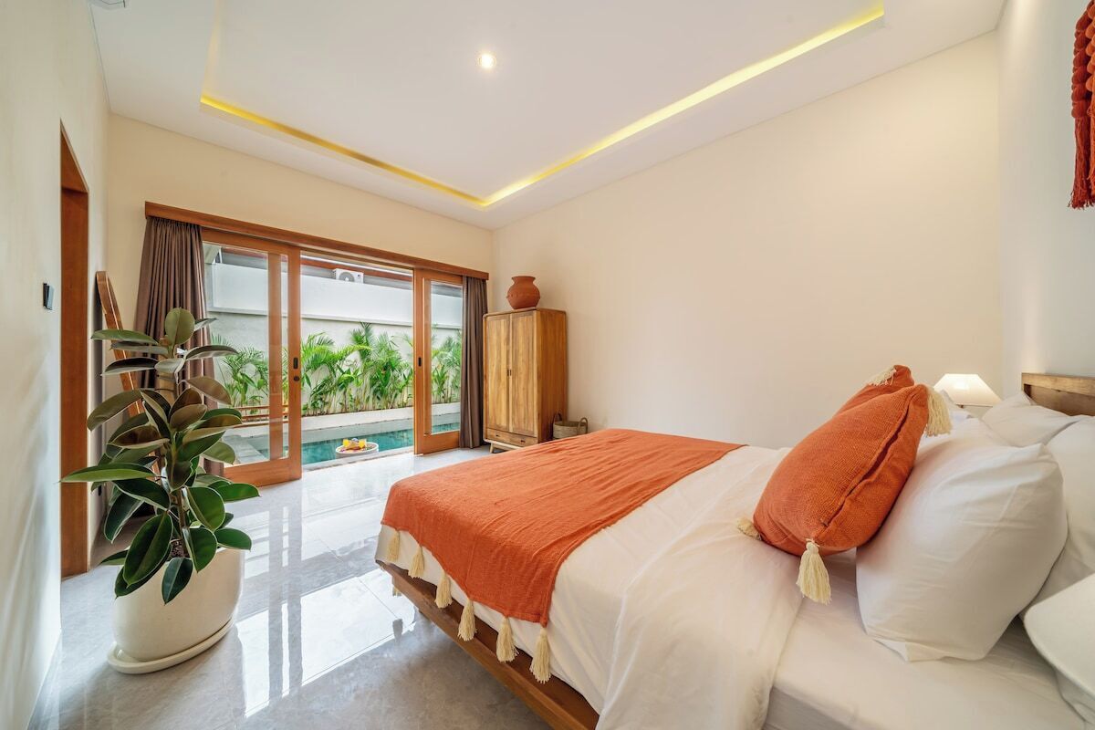 A hotel room with a bed, a potted plant, a wardrobe, and a view of a pool.