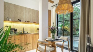 A modern kitchen with a wooden countertop, a dining area with a round table and chairs, and a large window with a view of greenery. - Cozy 1BR • Pool&Garden View • Patio • Central Ubud (Kabupaten Gianyar)