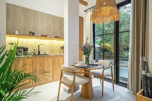 A modern kitchen with a wooden countertop, a dining area with a round table and chairs, and a large window with a view of greenery. - Cozy 1BR • Pool&Garden View • Patio • Central Ubud (Kabupaten Gianyar)