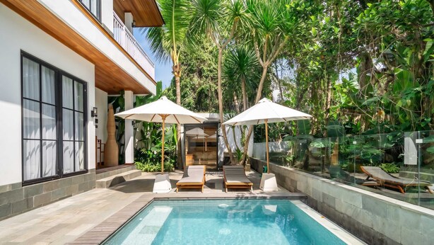 A modern outdoor pool area with lounge chairs and umbrellas, surrounded by lush greenery. - Cozy 1BR • Pool&Garden View • Patio • Central Ubud (Kabupaten Gianyar)