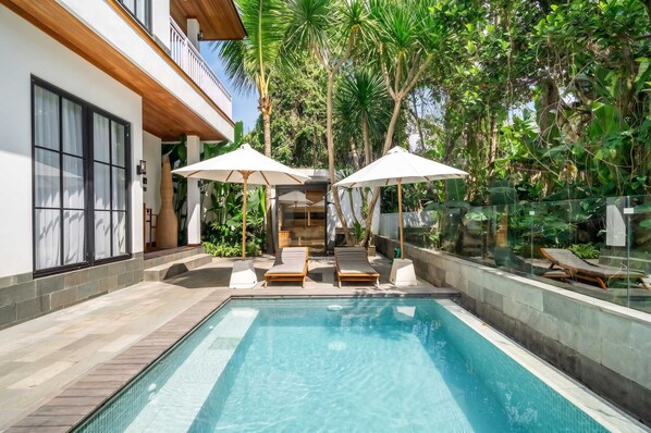 A modern outdoor pool area with lounge chairs and umbrellas, surrounded by lush greenery. - Cozy 1BR • Pool&Garden View • Patio • Central Ubud (Kabupaten Gianyar)