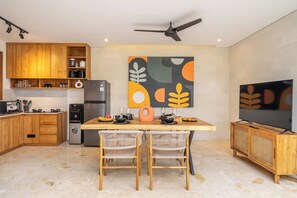 A modern kitchen with wooden cabinets, a dining table with two chairs, a refrigerator, and a flat-screen TV. - Paradise 2BR Villa w Beach Access & Private Pool (Kecamatan Kuta Utara)