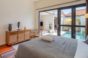 Een slaapkamer met een groot bed, een houten dressoir, een televisie en uitzicht op een zwembad.