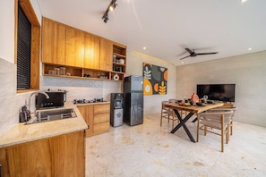 A modern kitchen with wooden cabinets, a built-in stove, a refrigerator, and a dining area with a TV and chairs. - Paradise 2BR Villa w Beach Access & Private Pool (Kecamatan Kuta Utara)