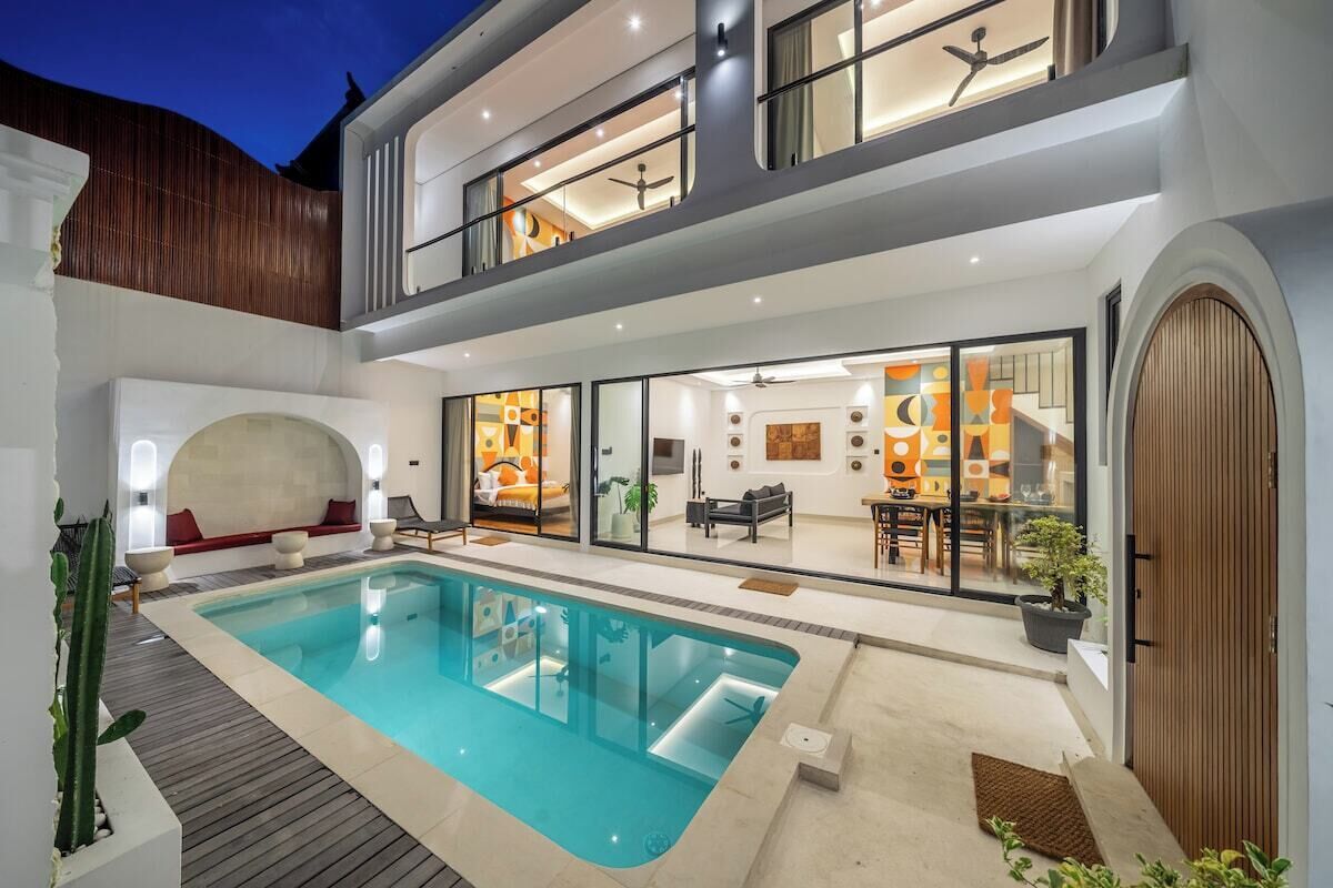 A modern two-story house with a swimming pool, outdoor seating, and a well-lit interior.