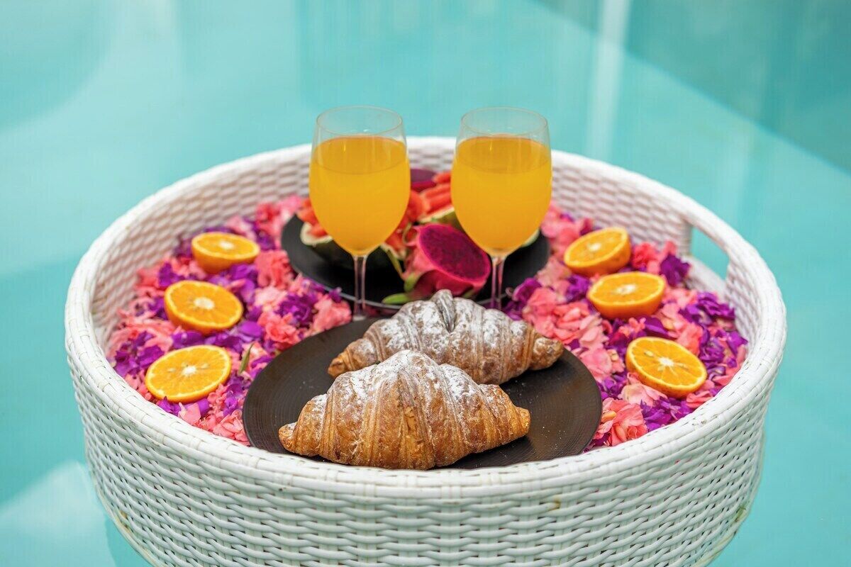 En korg av rotting som innehåller croissanter, apelsinskivor och två glas apelsinjuice, placerad på ett bord.