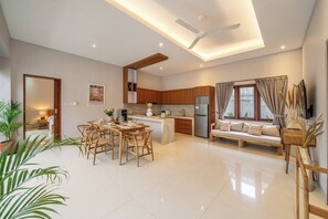 A modern kitchen with wooden cabinets, a dining area with a table and chairs, and a living area with a sofa and a TV. - Brand NEW Paradise Villa, Huge Pool, Canggu (Kabupaten Badung)