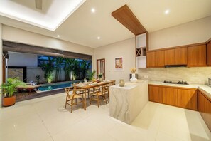 Een moderne keuken met houten kastjes, een marmeren aanrechtblad en een eethoek met uitzicht op een zwembad.