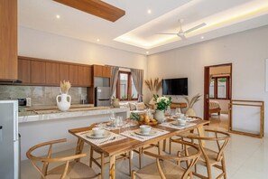 A modern kitchen with wooden cabinets, a dining area with a wooden table and chairs, and a flat-screen TV mounted on the wall. - Brand NEW Paradise Villa, Huge Pool, Canggu (Kabupaten Badung)